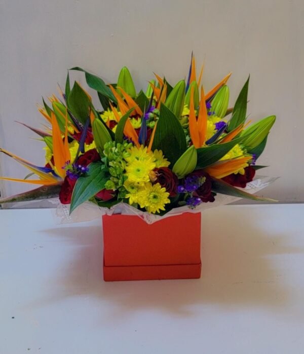 A vibrant floral arrangement featuring striking Bird of Paradise flowers, complemented by yellow chrysanthemums, purple blooms, and fresh green lilies in bud form. Presented in a bold red box, this arrangement exudes tropical elegance, making it a stunning choice for gifting or decoration.