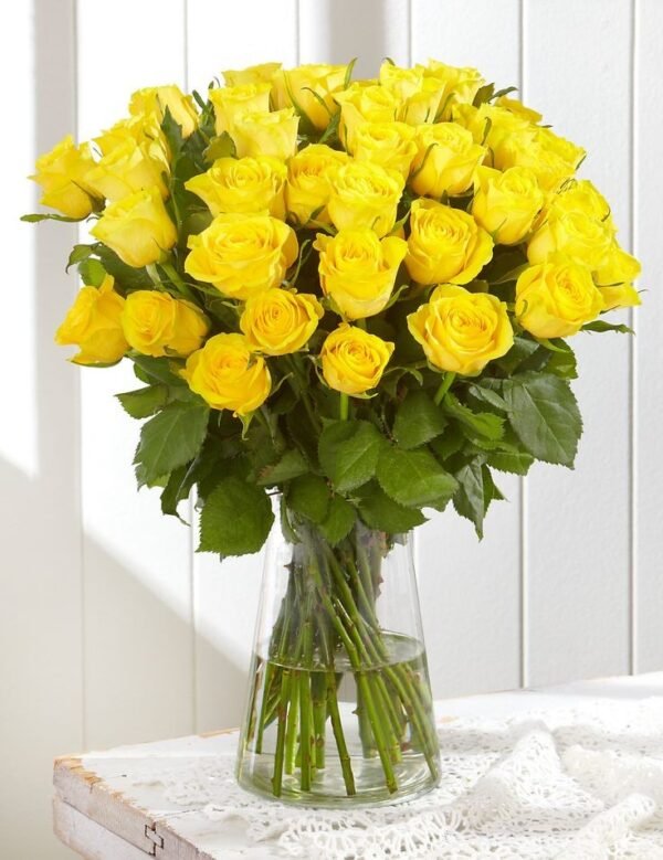 Vibrant bouquet of yellow roses arranged in a clear glass vase with lush green leaves, perfect for cheerful gifts and celebrations.