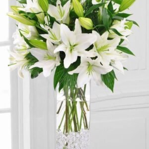 Stunning white lily bouquet in a tall glass vase with lush green foliage, ideal for elegant home decor and special occasions.