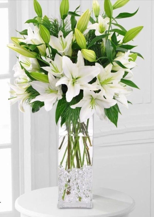 Stunning white lily bouquet in a tall glass vase with lush green foliage, ideal for elegant home decor and special occasions.