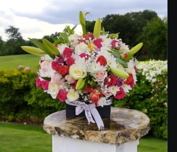 A stunning floral arrangement featuring a mix of red, white, and pink roses, complemented by fresh lilies and delicate baby’s breath. Presented in an elegant black box with a decorative ribbon, this bouquet exudes charm and sophistication, perfect for any special occasion.