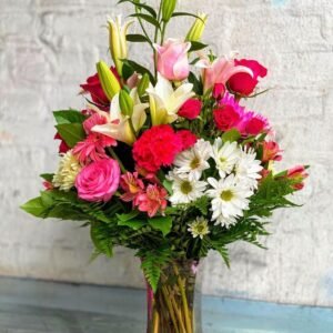 Elegant mixed flower bouquet in a glass vase featuring pink roses, white daisies, red carnations, and lilies, perfect for gifts and celebrations.