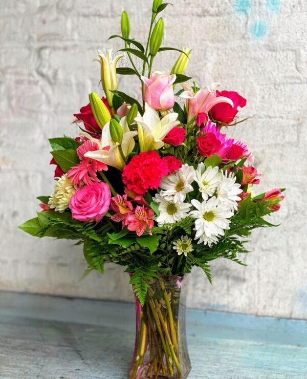 Elegant mixed flower bouquet in a glass vase featuring pink roses, white daisies, red carnations, and lilies, perfect for gifts and celebrations.