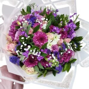 A beautiful bouquet featuring a mix of purple, pink, and white flowers, accented with lush greenery and delicate baby's breath, wrapped elegantly in white paper. A perfect choice for a romantic or celebratory occasion!