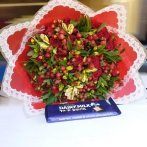 A stunning bouquet featuring a mix of red roses, hypericum berries, and delicate greenery, wrapped in decorative paper. Paired with a Dairy Milk Top Deck chocolate bar, this arrangement makes for a thoughtful and delightful gift, perfect for expressing love and appreciation.