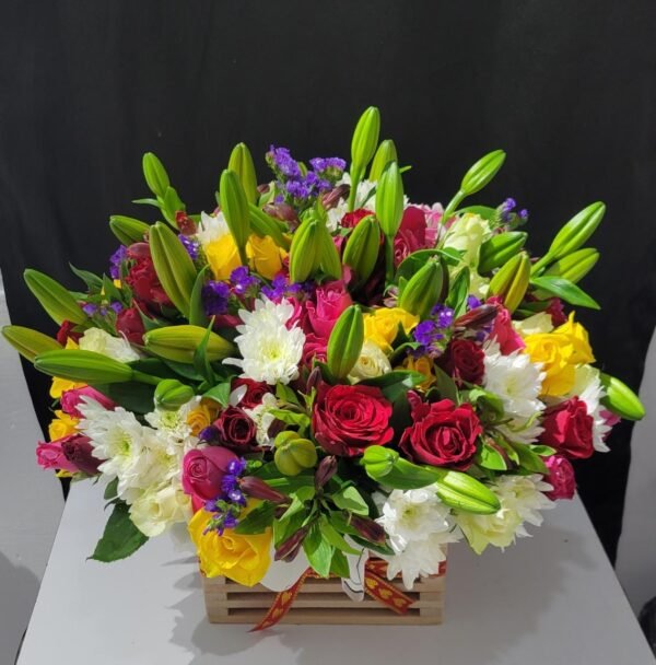 A vibrant floral arrangement featuring a mix of red roses, yellow roses, white chrysanthemums, purple flowers, and fresh green lilies in bud form. Set in a wooden crate with a decorative ribbon, this arrangement offers a stunning blend of colors and textures, making it an elegant choice for any special occasion or heartfelt gesture.