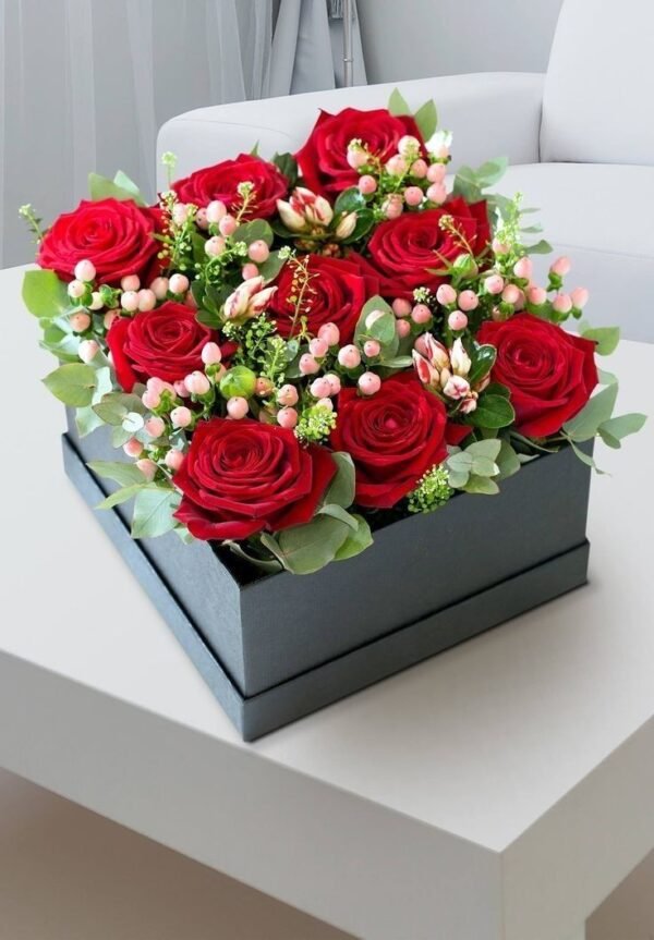 Box arrangement of red roses, pink berries, and greenery in a black gift box.
