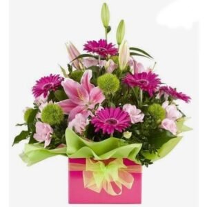 Floral arrangement of pink lilies, gerbera daisies, and greenery in a pink gift box with a green ribbon.