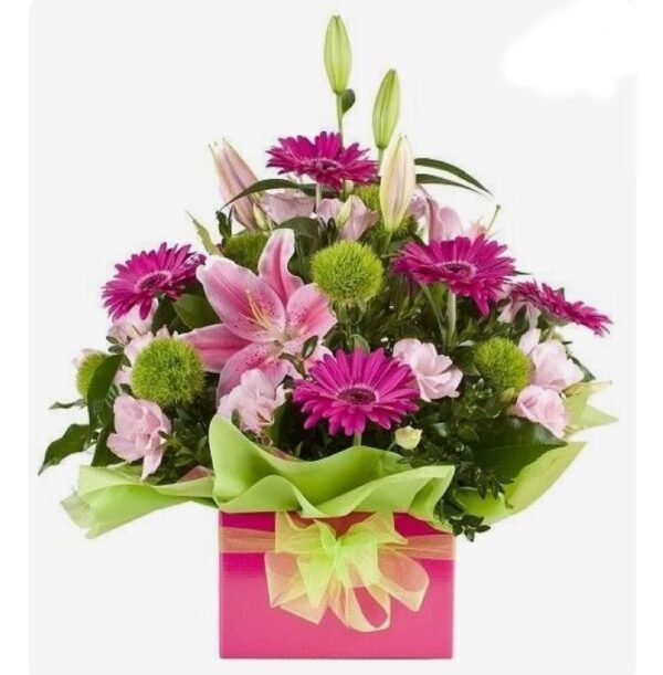 Floral arrangement of pink lilies, gerbera daisies, and greenery in a pink gift box with a green ribbon.