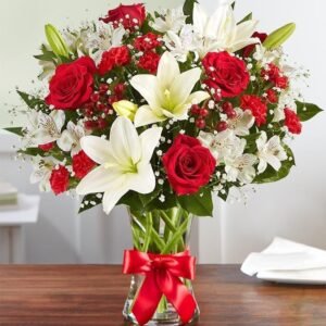 Elegant bouquet of red roses, white lilies, alstroemeria, and baby's breath, arranged in a glass vase with a red ribbon.