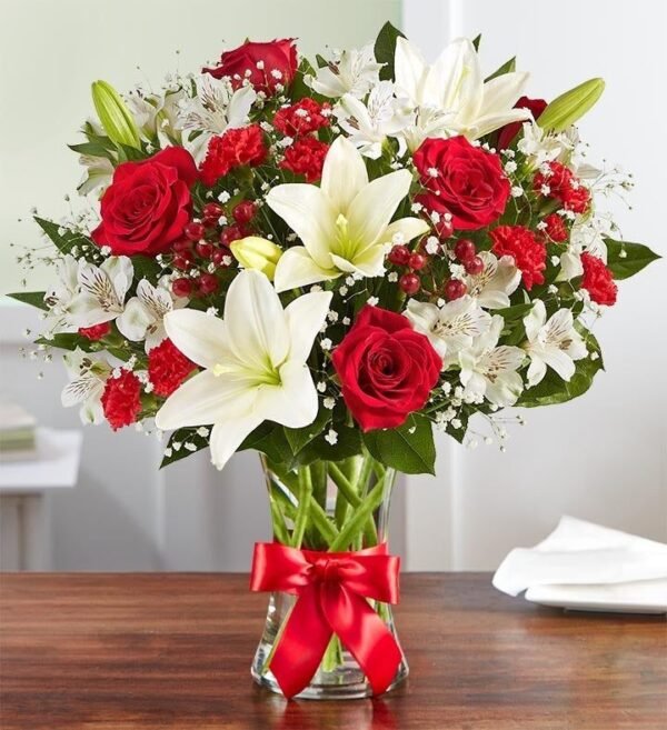 Elegant bouquet of red roses, white lilies, alstroemeria, and baby's breath, arranged in a glass vase with a red ribbon.