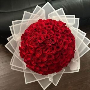 Luxurious bouquet of tightly packed red roses wrapped in elegant white translucent paper.