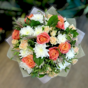 Charming bouquet of peach roses, white chrysanthemums, and delicate greenery, wrapped in soft pastel paper.