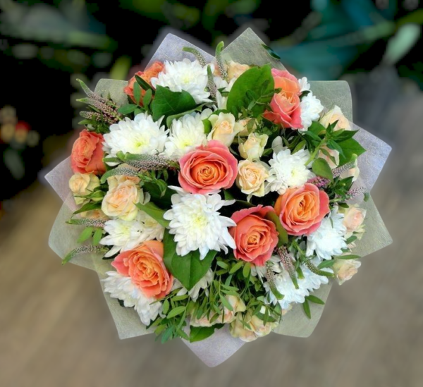 Charming bouquet of peach roses, white chrysanthemums, and delicate greenery, wrapped in soft pastel paper.