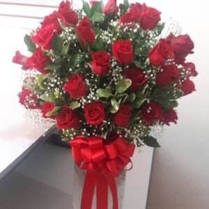 Luxurious bouquet of red roses with baby's breath and lush greenery, arranged in a glass vase with a red ribbon.